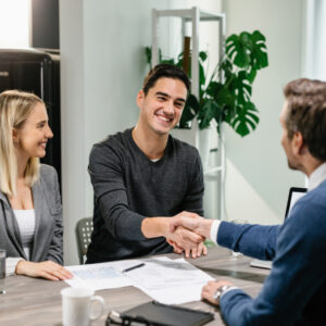 young-happy-couple-making-agreement-with-their-financial-advisor-home-men-are-shaking-hands 1